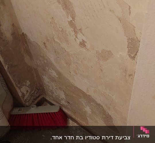 קיר מתקלף עם מטאטא וחתיכות צבע על הרצפה